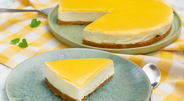 En krämig cheesecake med en syrlig lemon curd-topping. En bit serverad på en tallrik bredvid en hel cheesecake.