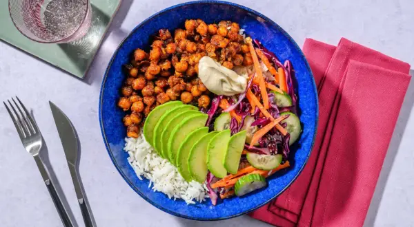 En blå skål med ris, kryddiga kikärtor, avokado, gurka, morot och rödkål. Ett perfekt bowls recept för en snabb och god middag.