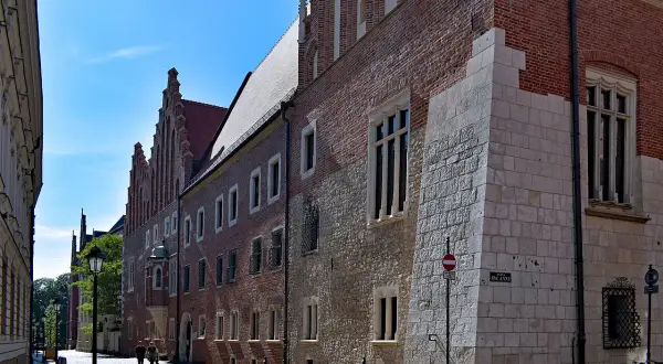 Kamienne i ceglane mury Collegium Maius w Krakowie, z charakterystycznymi oknami i detalami architektonicznymi, na tle błękitnego nieba.