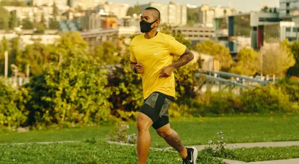 Man running with oxygen mask on a path, city skyline in background.