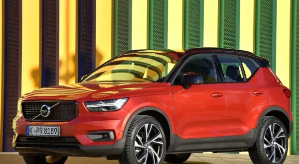 Czerwone Volvo XC40 na tle kolorowej ściany. Wiele osób szuka volvo xc40 opinie przed zakupem.