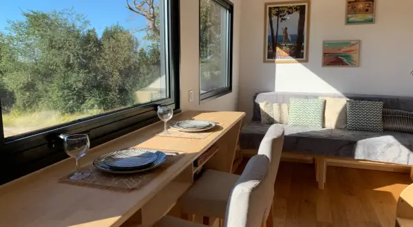 Intérieur d'une tiny house dans les Landes, avec un coin repas face à la nature et un canapé confortable.