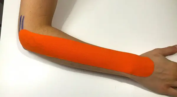 Pomarańczowy plaster kinezjotaping na przedramieniu, wspierający ćwiczenia na łokieć tenisisty.