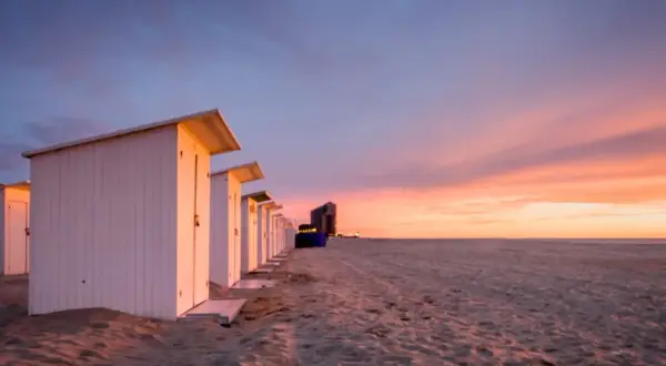Strandkabinen am Meer bei Sonnenuntergang mit dramatischem Himmel.