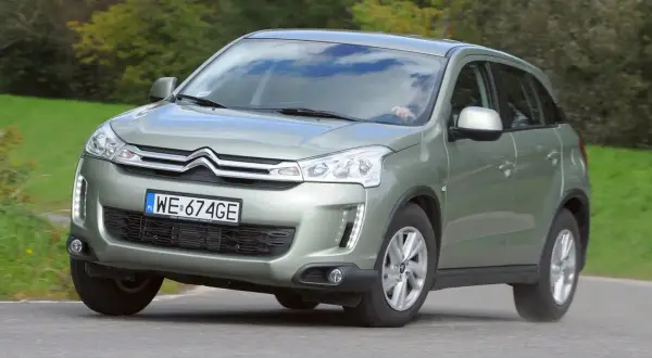 Zielony Citroen C4 Aircross z polskimi tablicami WE 674GE jedzie po drodze wśród zieleni.