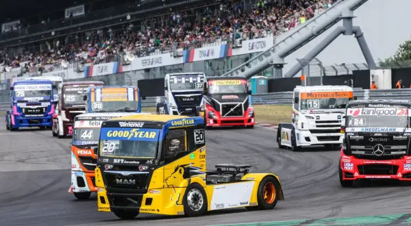 Des camions de course colorés s'affrontent lors d'un grand prix camion, sous les yeux d'une foule en délire dans les tribunes.