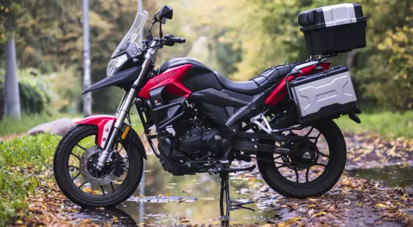 Czerwony motocykl turystyczny z kuframi, zaparkowany na jesiennej drodze. Model kat a1 gotowy na przygodę.