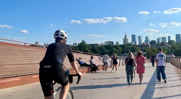 Rowerzysta na trasie rowerowej wzdłuż Wisły w Warszawie, z widokiem na panoramę miasta.