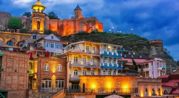Tbilisi, stolica Gruzji, nocą. Zabytkowe budynki z kolorowymi balkonami i twierdza na wzgórzu.