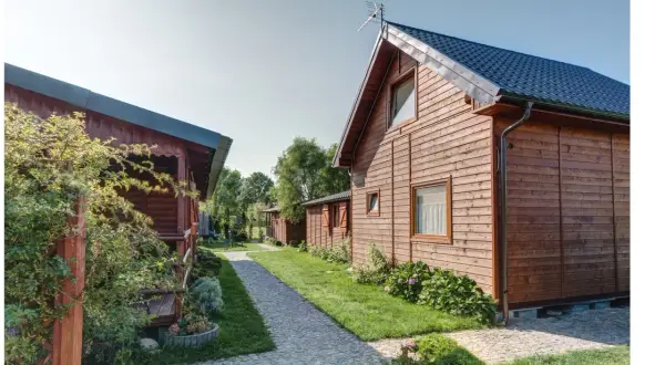 Drewniane domki letniskowe, idealne na wicie nad morzem. Ścieżka z kostki brukowej prowadzi między zielonymi trawnikami a budynkami.