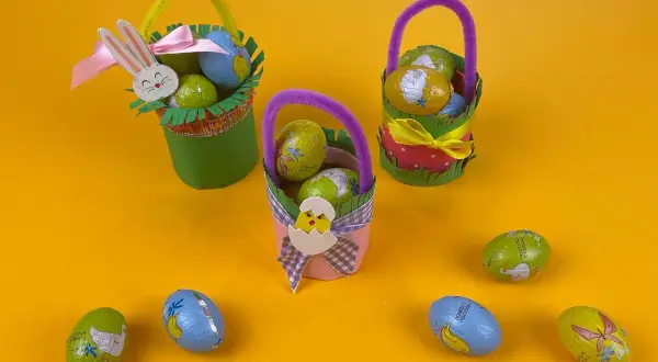 Tre cestini di Pasqua fai da te, decorati con coniglietti e pulcini, pieni di uova di cioccolato.