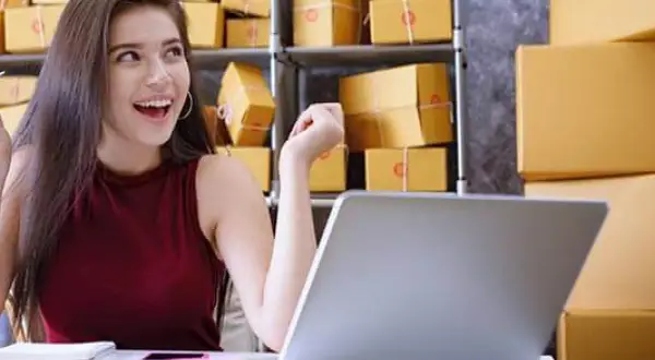 Szczęśliwa młoda kobieta przy laptopie, otoczona paczkami. To inspiracja, jak zacząć dropshipping i rozwijać swój biznes online.