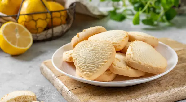 Deliziosi biscotti senza burro a forma di cuore e rotondi, serviti su un piatto bianco con limoni freschi sullo sfondo.