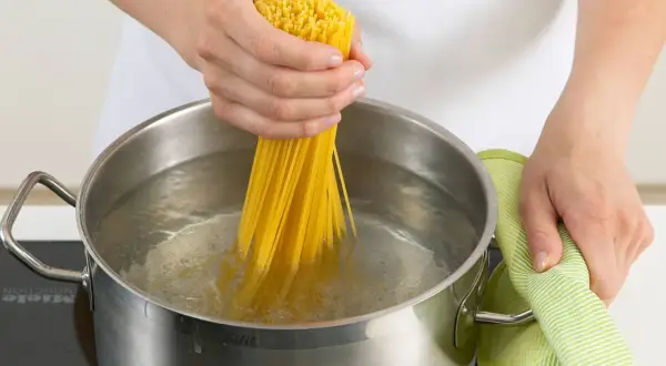 Hände halten Spaghetti, um sie in kochendes Wasser zu geben. Nudeln kochen ohne Herd ist hier nicht zu sehen, aber das Wasser brodelt.