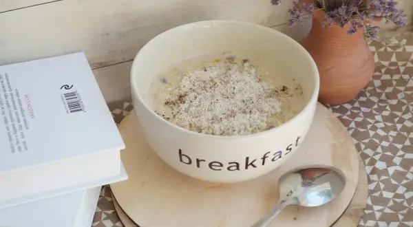 Misternie przygotowana owsianka na śniadanie, a obok książka. Czy płatki owsiane mają gluten? To pytanie nurtuje wielu.