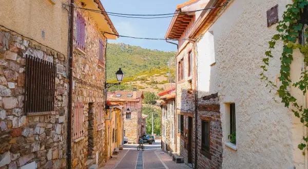 Calle empedrada en Puebla de la Sierra que ver. Casas de piedra y tejados rojos, con colinas verdes al fondo.