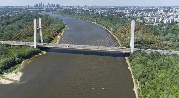 Most Siekierkowski w Warszawie nad Wisłą, z widokiem na panoramę miasta i zielone brzegi.