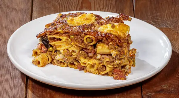 Porzione di pasta ncasciata ricca e saporita, con rigatoni, ragù, uova e verdure, servita su un piatto bianco.