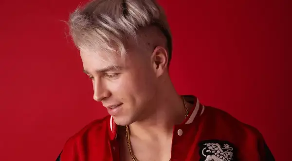 Młody mężczyzna z blond włosami i złotym łańcuchem na szyi, w czerwonej kurtce. Ile lat ma Skolim?