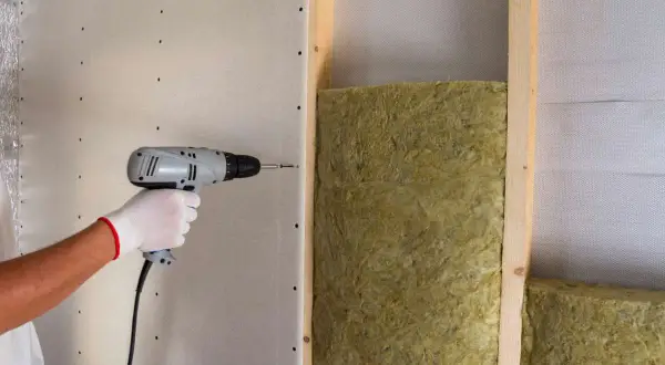 Instalación de aislamiento para como aislar una pared del ruido de los vecinos. Se atornilla placa de yeso sobre estructura de madera con lana mineral.