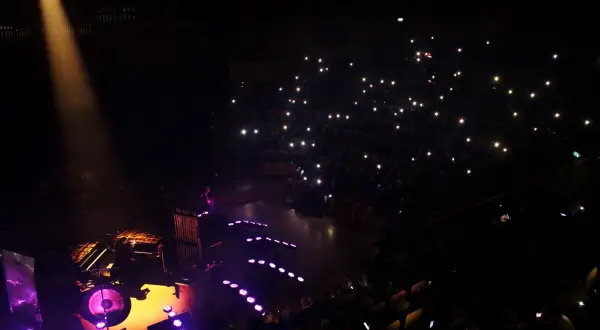 Koncert w ciemności: scena z muzykami, publiczność z zapalonymi telefonami.