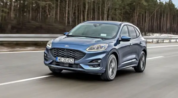 Niebieski Ford Kuga z silnikiem 1.5 Ecoboost pędzi po autostradzie wśród drzew.