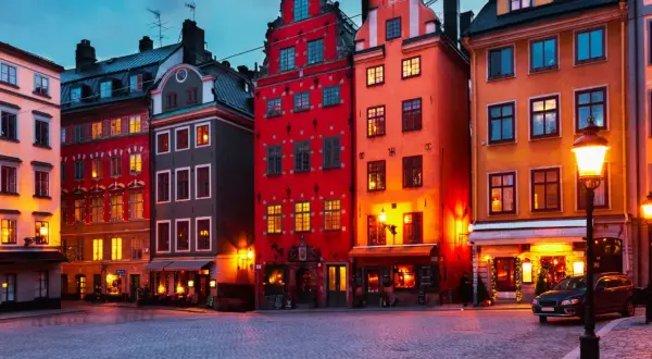 Färgstarka hus i **altstadt Stockholm** lyser upp en kullerstensbelagd gata i skymningen.
