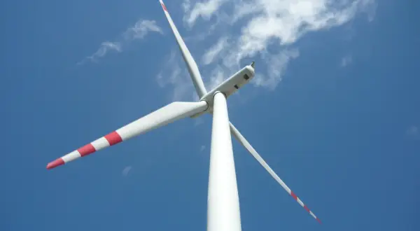 Biała mała elektrownia wiatrowa z czerwonymi pasami na łopatach obraca się na tle błękitnego nieba z chmurami.