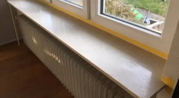 Un nouveau rebord de fenêtre en pierre, prêt à accueillir des plantes, surplombe un radiateur blanc.