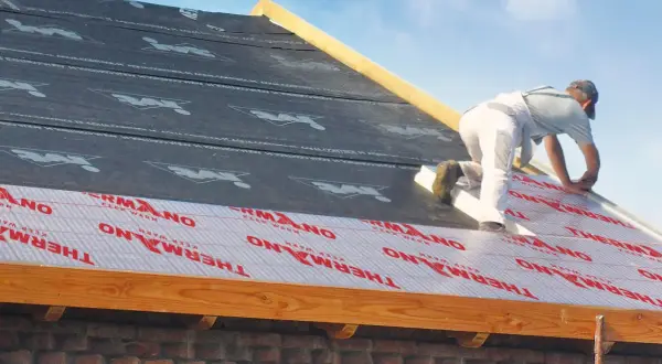 Pracownik montuje ocieplenie nakrokwiowe na dachu, układając warstwy izolacji i membrany.