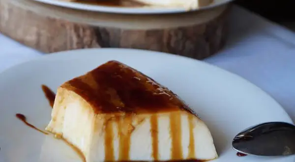 Un trozo de tarta de cuajada, cubierto de caramelo líquido, reposa en un plato blanco.