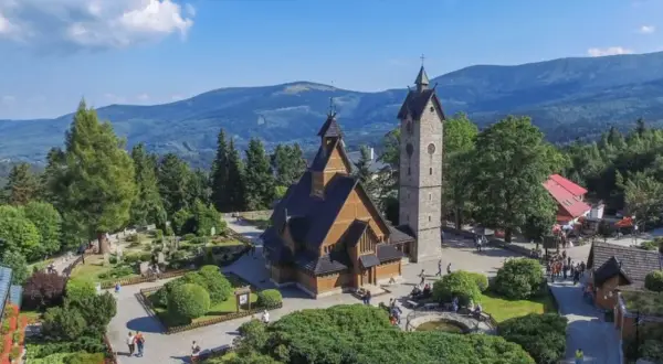 Drewniany kościółek i wieża na tle górskich krajobrazów. Czy to Karpacz, czy Szklarska Poręba?