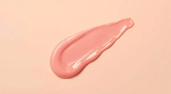 En rosa, glansig sträng av pdrn serum på en ljusrosa bakgrund.