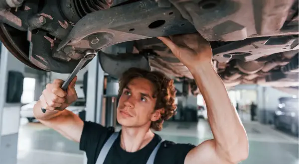 Mechanik naprawia zawieszenie auta, podejrzewając jazdę z uszkodzoną tuleją wahacza.