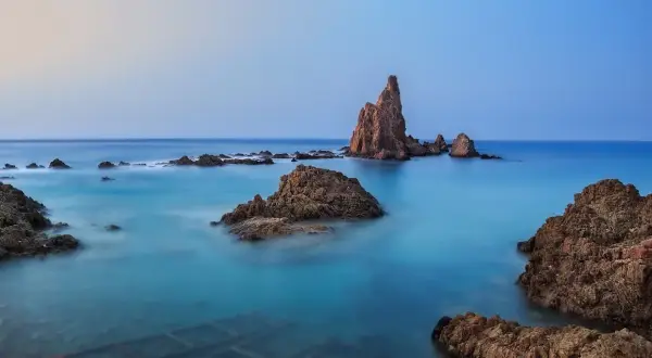 Rocas emergiendo de aguas turquesas en el fondo marino de Cabo de Gata. El cielo se funde con el mar en un amanecer sereno.