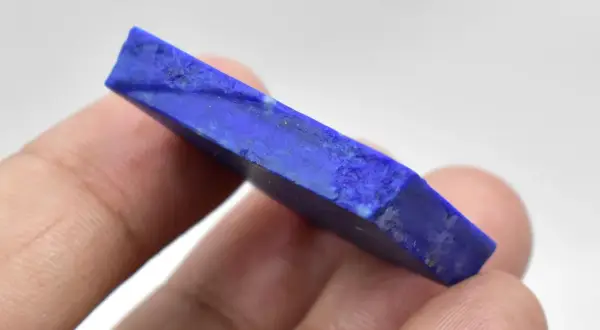 Królewski lapis lazuli, kamień o intensywnym niebieskim kolorze, trzymany w palcach.