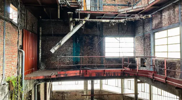 Intérieur d'une usine abandonnée, typique d'un site d'urbex dans la Somme. Structures métalliques rouillées, tuyaux, briques apparentes et lumière filtrant par les fenêtres.