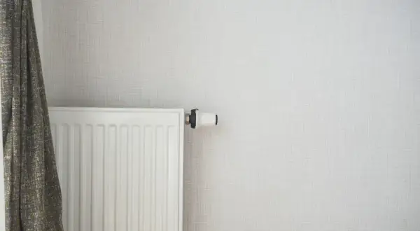 Radiateur blanc moderne, prêt à être alimenté par une pompe à chaleur. Un rideau discret complète la scène.