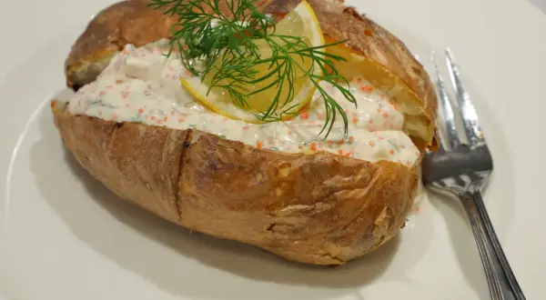 En saftig bakad potatis fylld med en krämig röra med rom, dill och citron. En gaffel ligger bredvid.