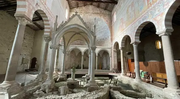 Interno della Basilica di San Piero a Grado, con affreschi medievali e resti archeologici al centro.