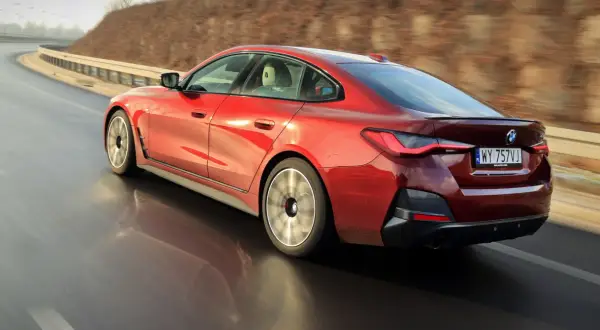 Czerwone BMW 4 Gran Coupé pędzi po zakręcie drogi, odbijając się w mokrej nawierzchni.