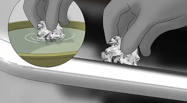 Mano con guanto pulisce con carta stagnola una cromatura rovinata, immergendola prima in un liquido.