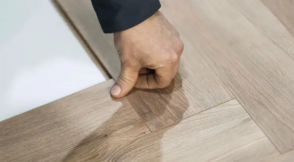 Dłoń precyzyjnie układa panele w jodełkę, tworząc elegancką podłogę.