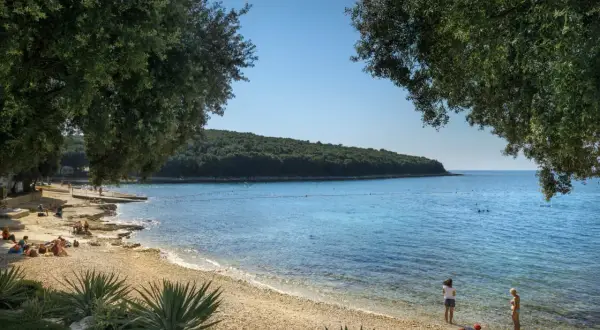 Słoneczny dzień na plaży w Porto Sole. Ludzie odpoczywają na kamienistym brzegu, a w krystalicznie czystej wodzie widać kąpiących się.