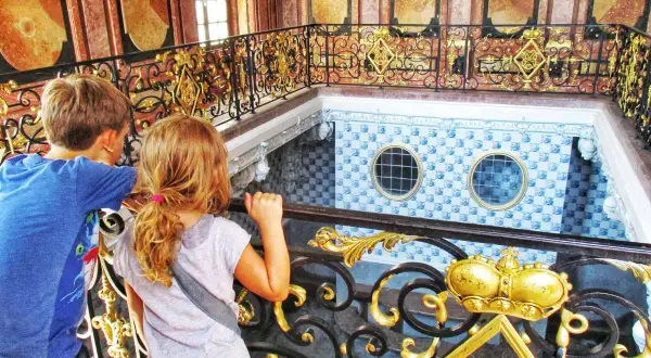 Kinder blicken auf die prunkvolle Treppe im Badenburg Nymphenburg.