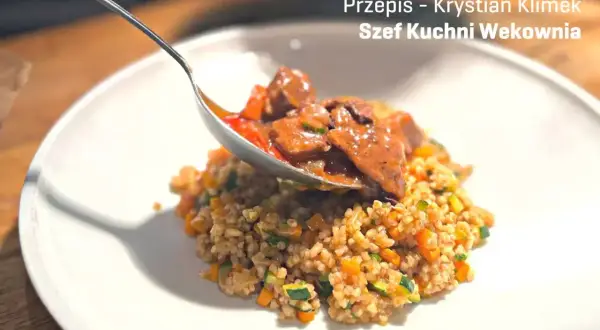 Gulasz z dzika z kaszotto warzywnym. Łyżka nakłada aromatyczne mięso na talerz pełen zdrowego kaszotto.