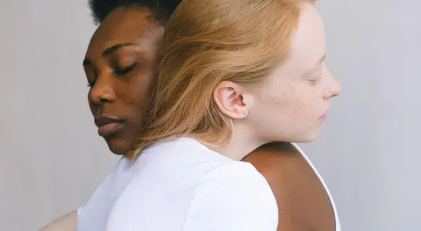 Twee vrouwen, één met donkere huid, de ander met lichte huid, omhelzen elkaar. Een beeld van verbinding, dat het verschil tussen compassie en empathie illustreert.