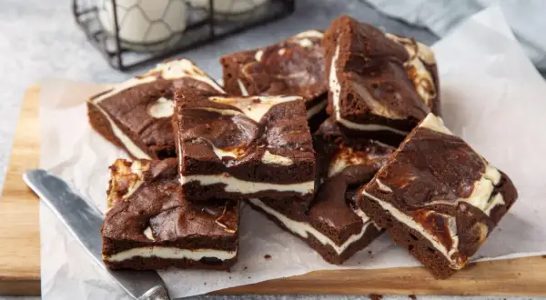 Szybkie ciasto z serem z wiaderka, czekoladowe brownie z kremową warstwą sera, ułożone na desce.