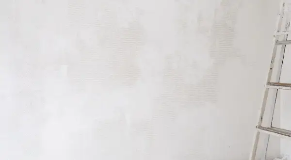 Étape de nettoyage d'un mur blanc jauni, une échelle est visible sur la droite.