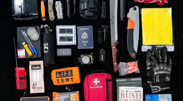 Un conjunto de herramientas EDC para supervivencia: pala plegable, cuchillos, linterna, multiherramienta, pistola, brújula, kit de primeros auxilios, sierra, manta térmica, guantes, libro de supervivencia y más.